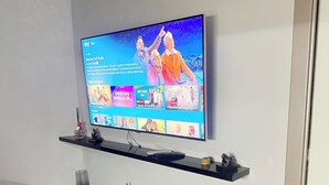 A flat-screen TV mounted on a wall above two black shelves.