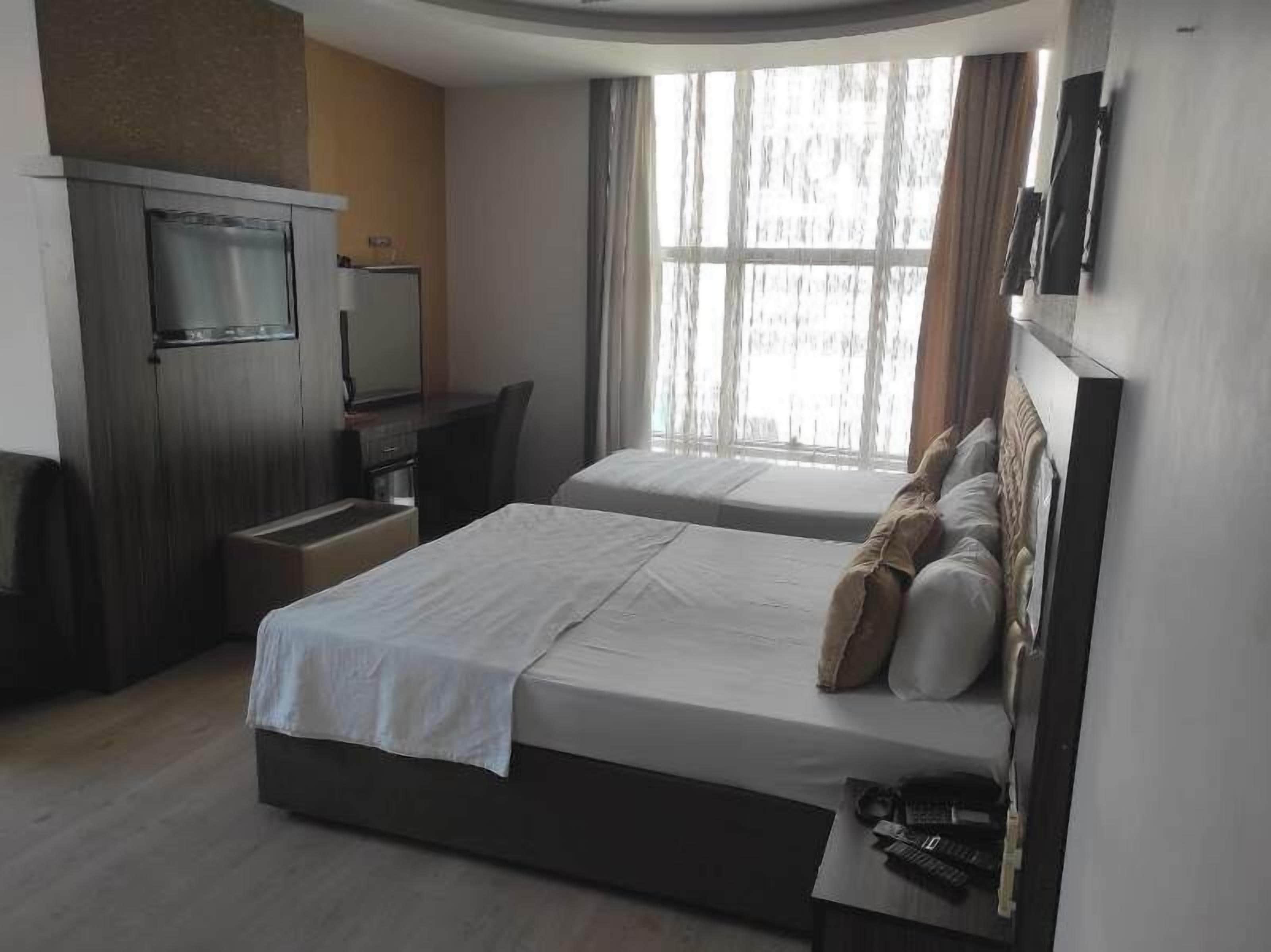 A hotel room with two beds, a desk, a TV, and a large window.