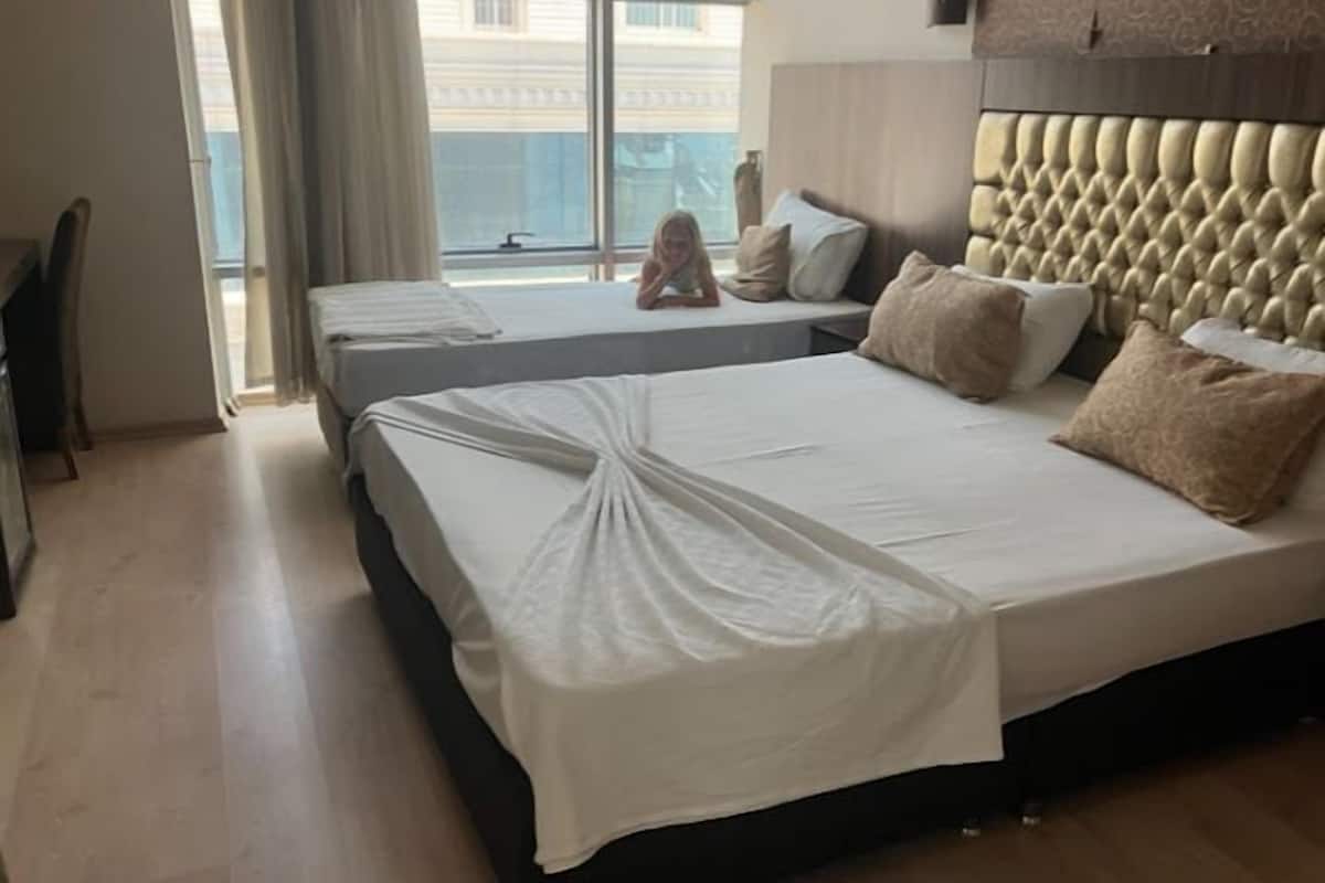A hotel room with two beds, a large window, and a view of buildings outside.