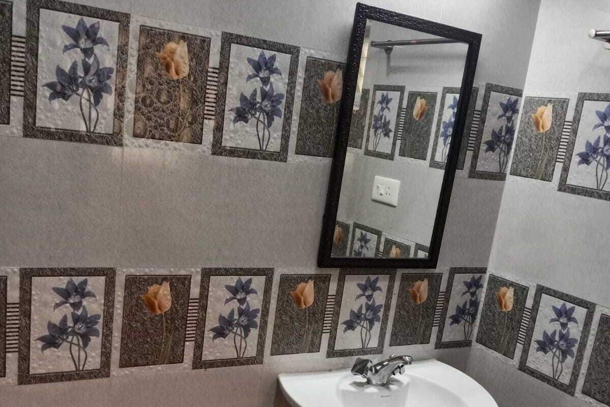 Ein Badezimmer mit einem weißen Waschbecken, einem Spiegel und dekorativen Fliesen mit floralen Mustern.