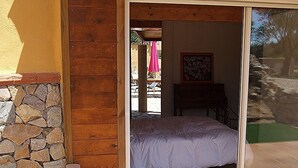 Een slaapkamer met een bed, een stenen muur en een houten deur die uitkomt op een buitenruimte met een tafel en stoelen.