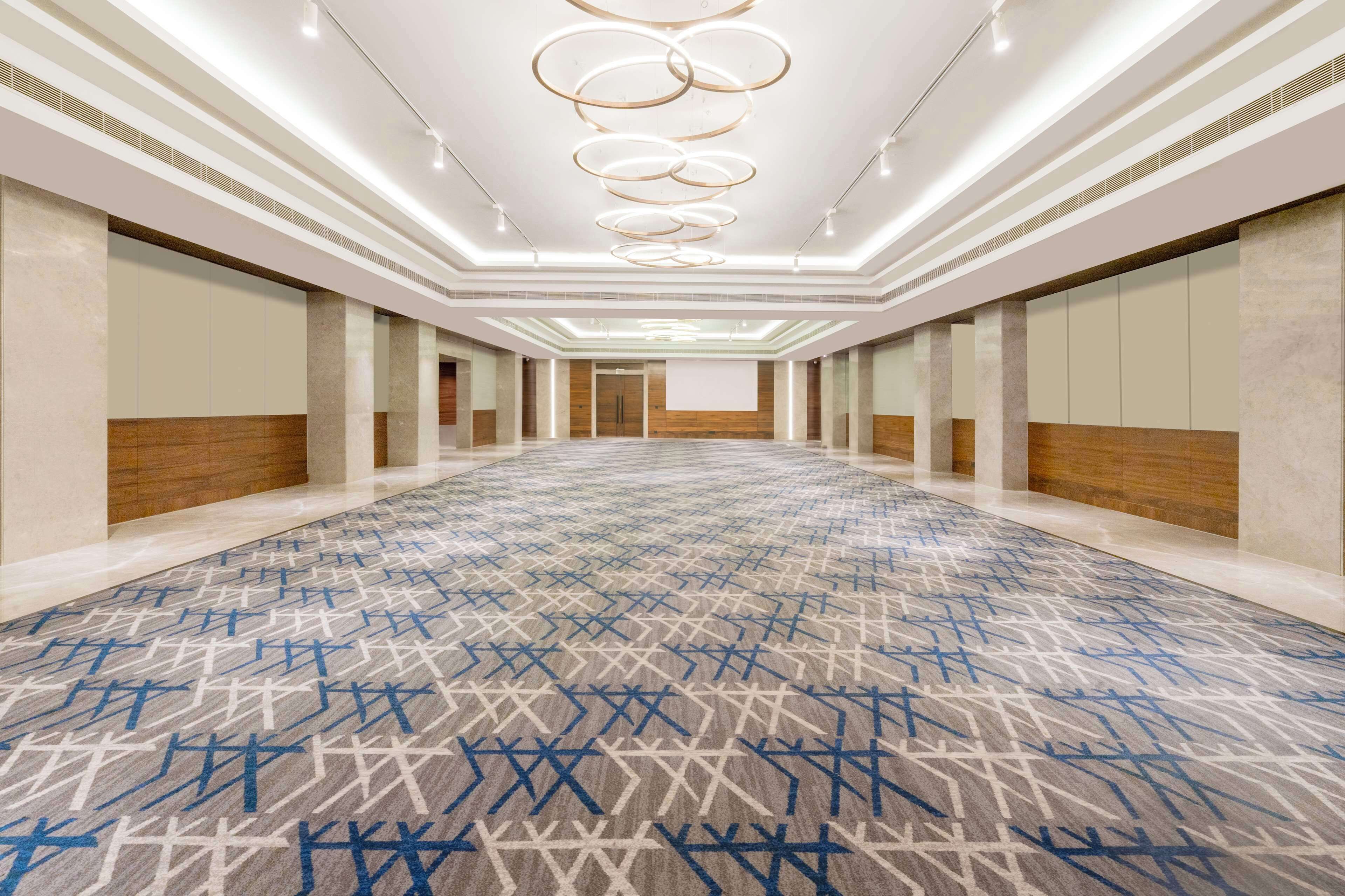 Un vestíbulo de hotel espacioso con alfombra estampada, un largo pasillo y una pantalla grande al final.