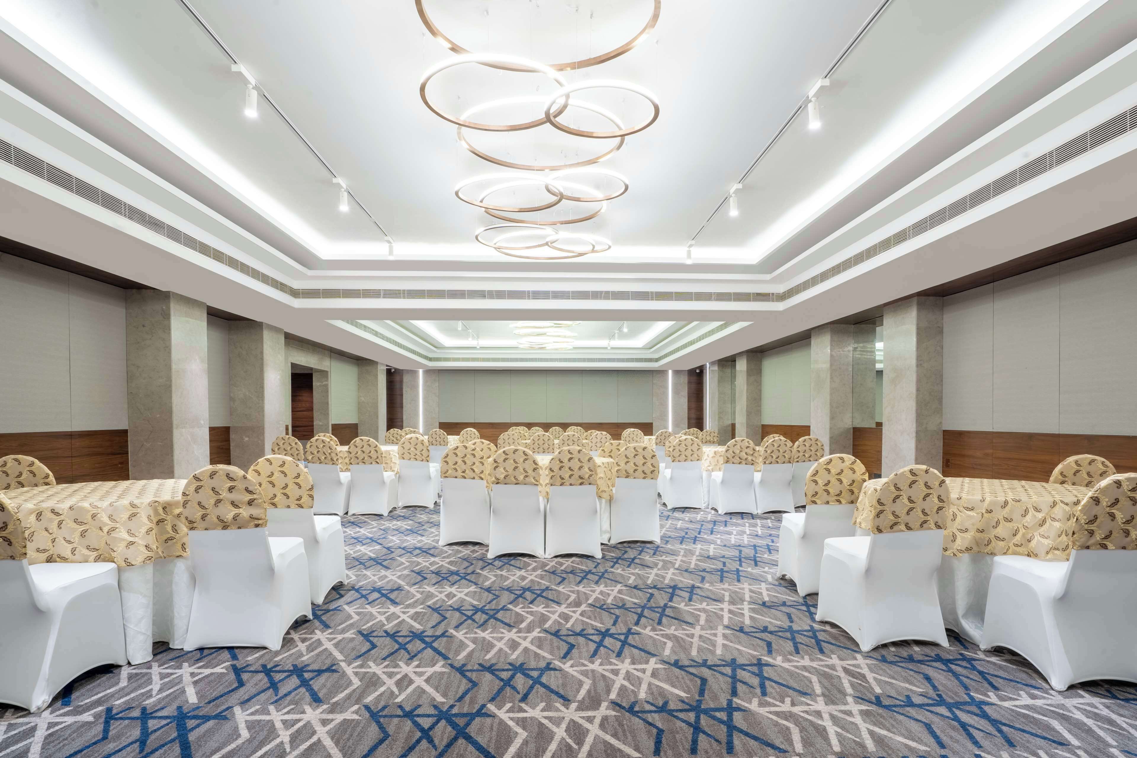 Une salle de conférence avec des rangées de chaises blanches, des repose-têtes beiges et une moquette à motifs.