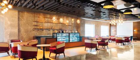 Een ruime lobby met modern meubilair, een centraal display en een plafond met zichtbare balken en hanglampen.