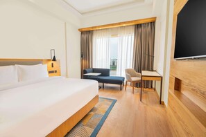 A hotel room with a large bed, a desk, a chair, a TV, and a view of the outdoors. - Radisson Hotel Vrindavan (Mathura)