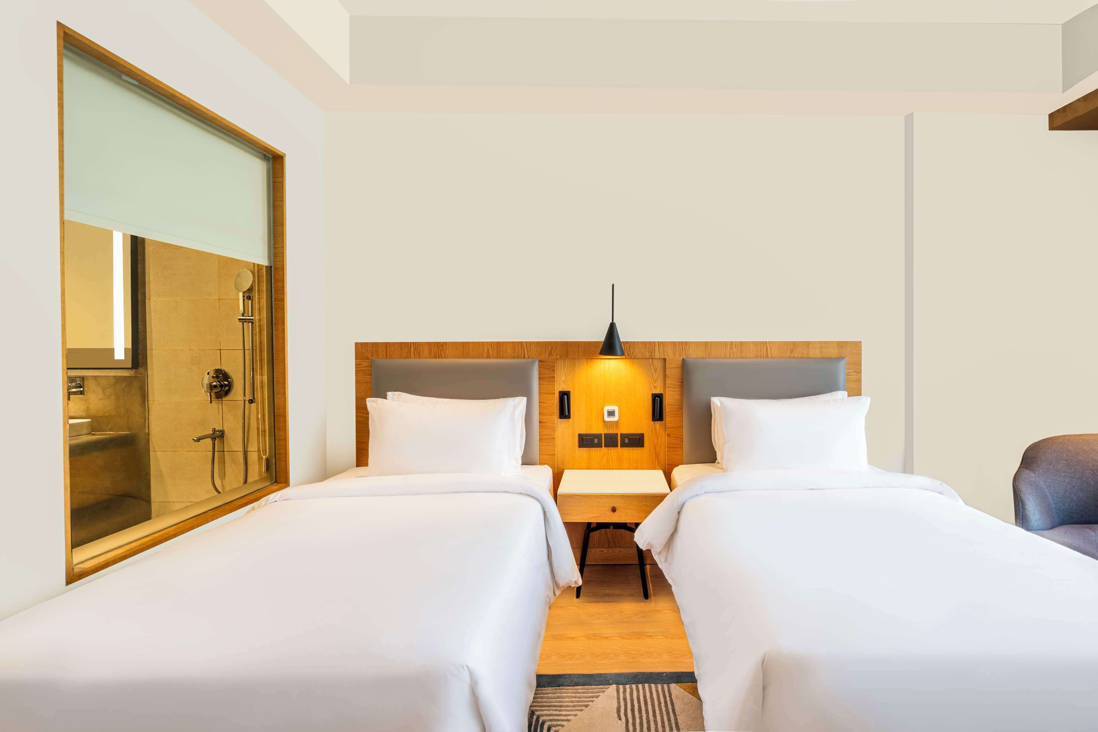 A hotel room with two beds, a wooden headboard, a nightstand, a mirror, and a shower area.