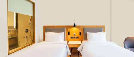 A hotel room with two beds, a wooden headboard, a nightstand, a mirror, and a shower area.