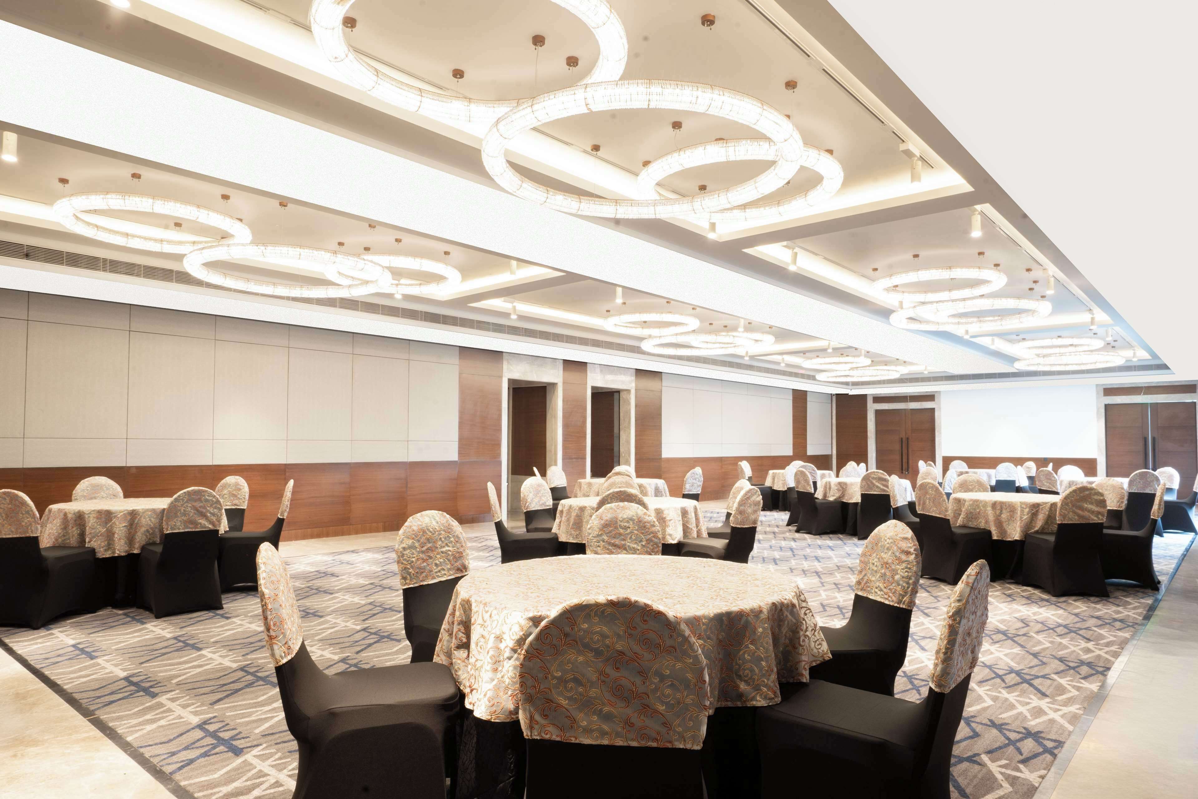 A conference room with round tables and chairs, ceiling lights, and a patterned carpet.