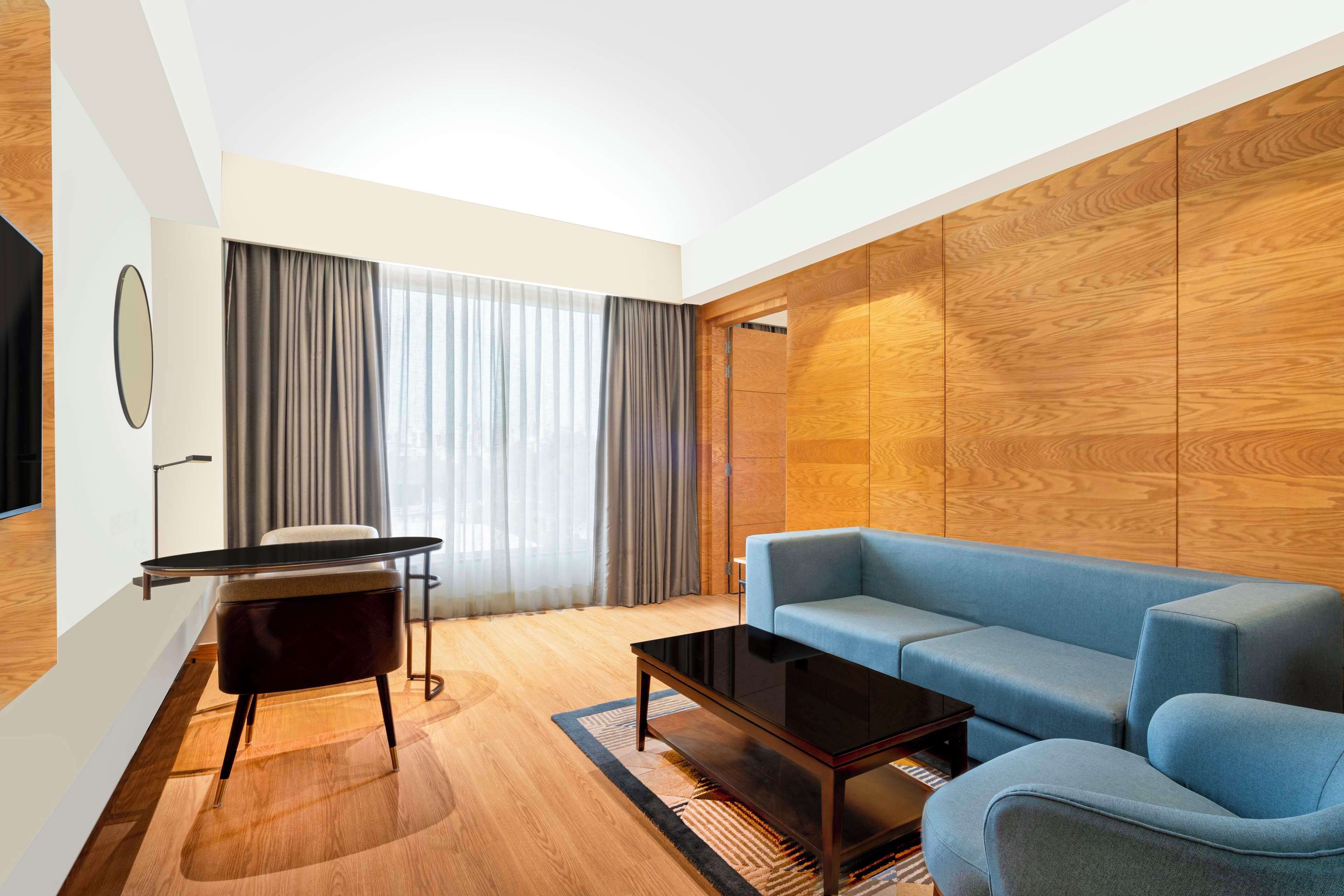 A modern living room with a blue sofa, a glass coffee table, and a wooden accent wall.