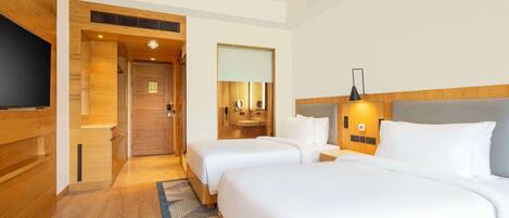 A hotel room with two beds, a television, a bathroom with a mirror, and a wooden floor.