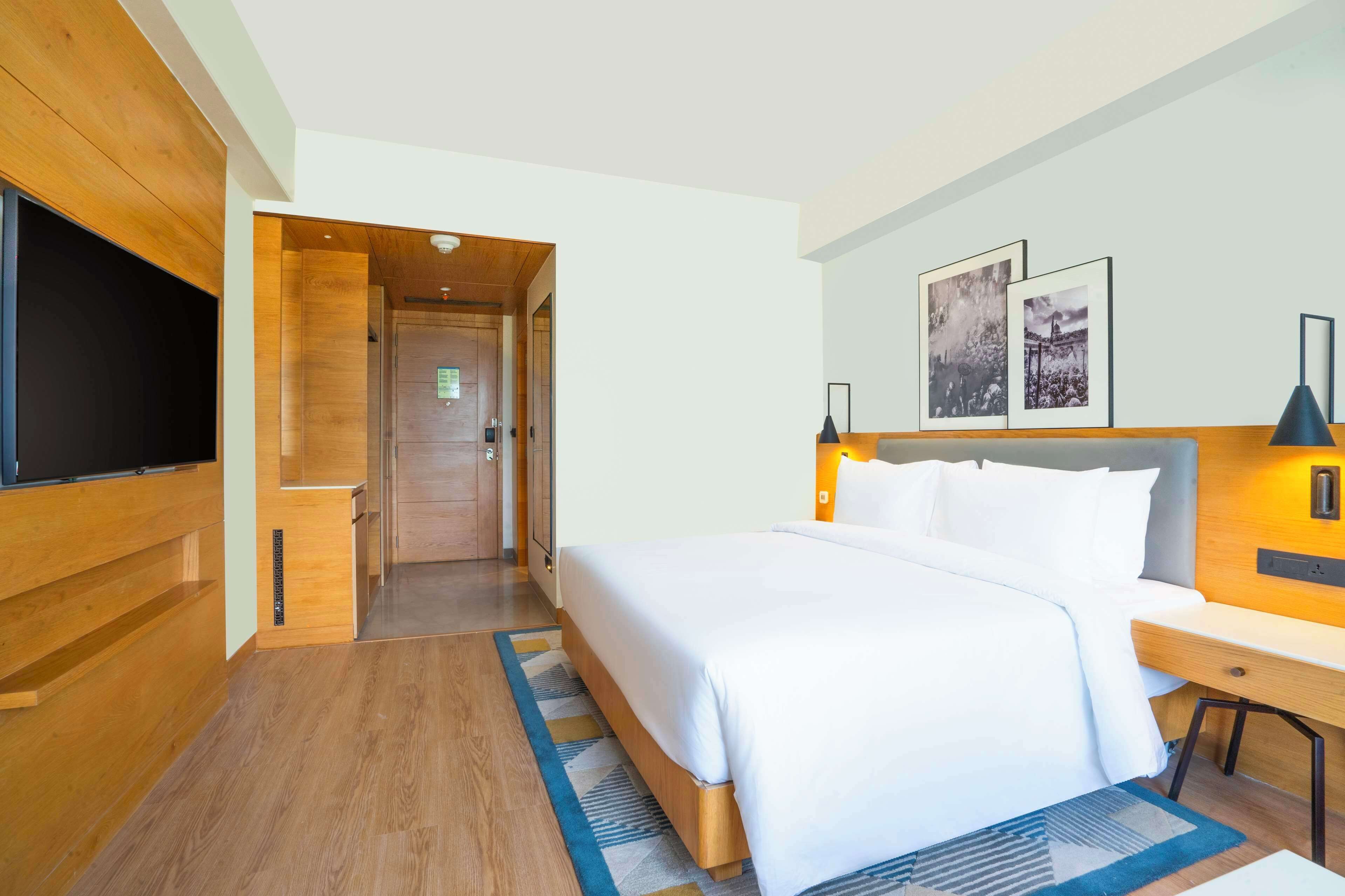 Habitación de hotel con una cama grande, televisión, paneles de madera y dos cuadros en la pared.