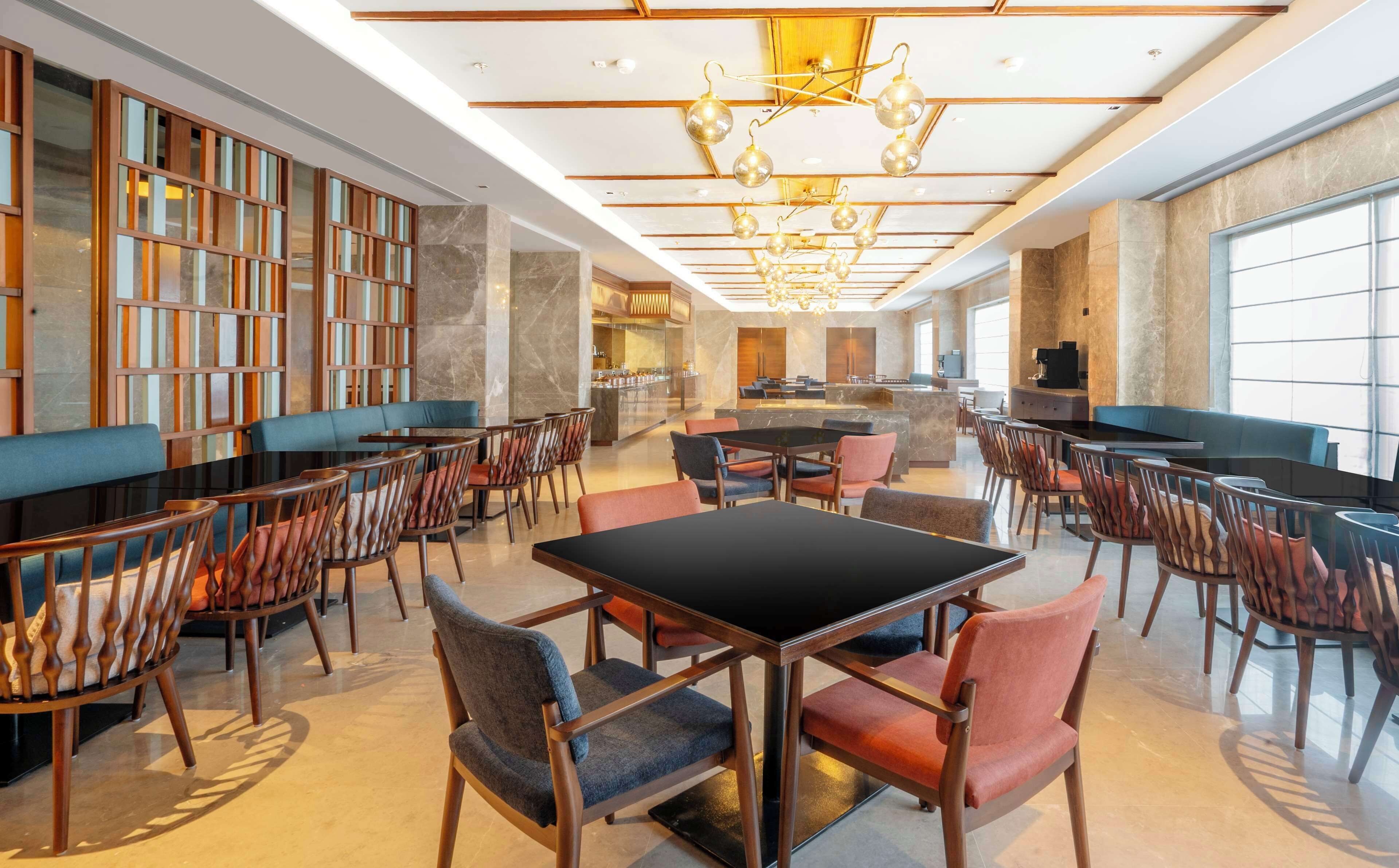 A spacious hotel lobby with a central seating area, a bar, and a large window providing natural light.