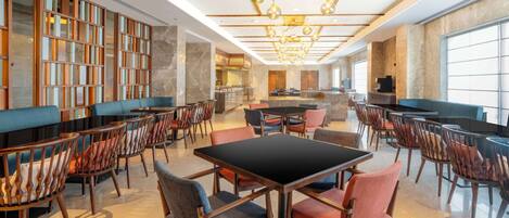 A spacious hotel lobby with a central seating area, a bar, and a large window providing natural light.