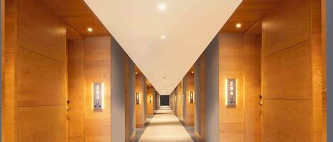 Un largo pasillo estrecho con paredes de madera y puertas numeradas, que conduce a un extremo luminoso y bien iluminado.