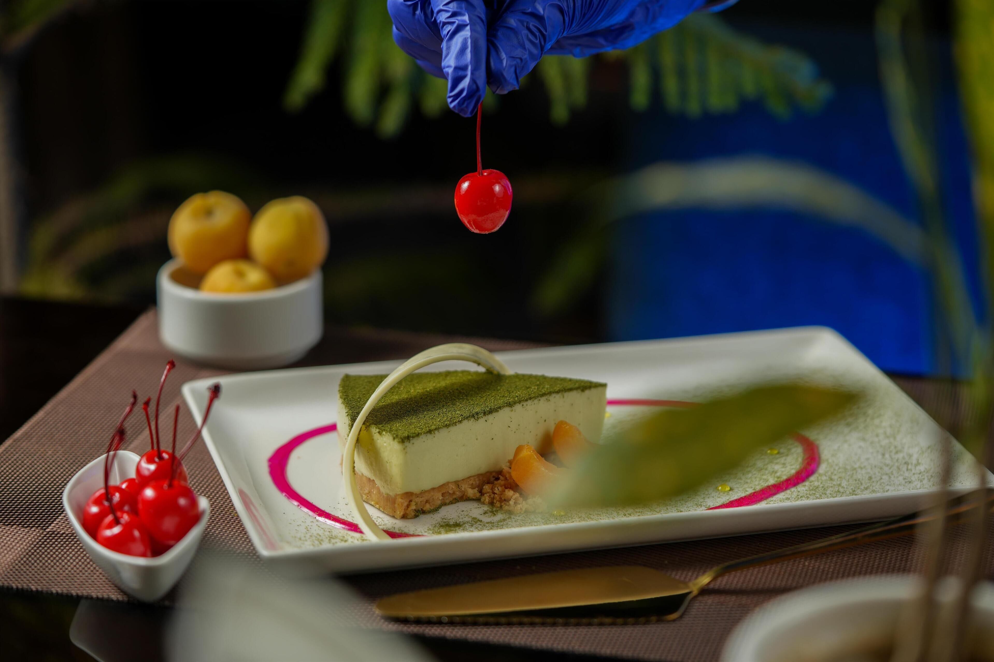 A dessert plate with a slice of cake, a bowl of cherries, and a bowl of lemons.