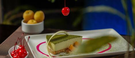 A dessert plate with a slice of cake, a bowl of cherries, and a bowl of lemons.