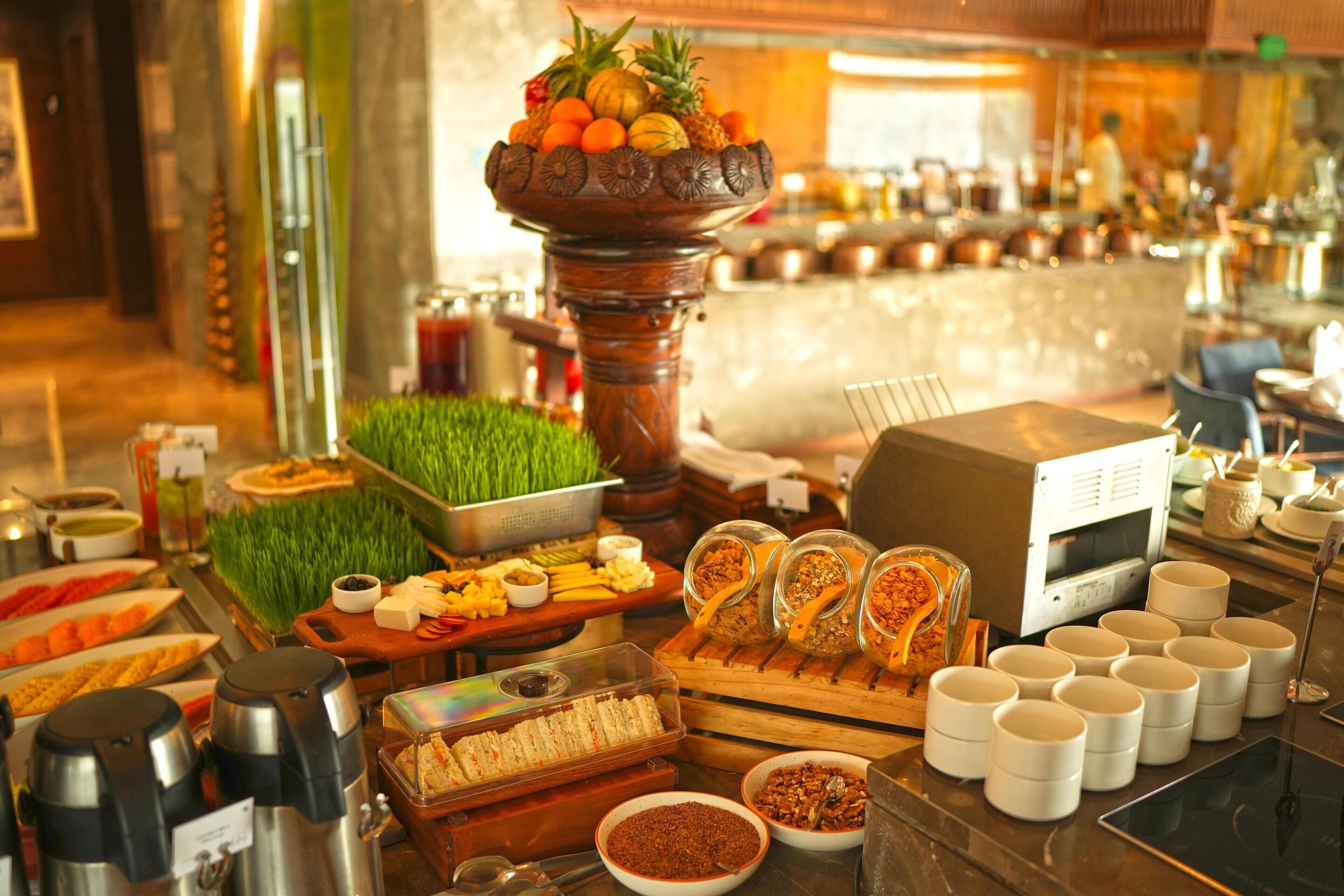 A buffet with various food items, a coffee machine, and a decorative centerpiece with fruits and vegetables.