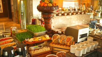 A buffet with various food items, a coffee machine, and a decorative centerpiece with fruits and vegetables.