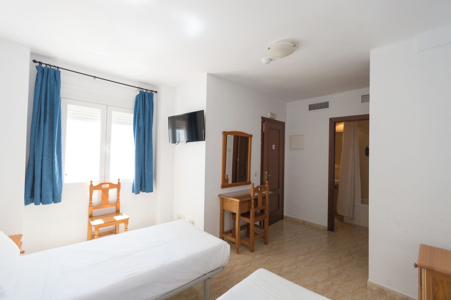 A bedroom with a bed, a desk, a chair, a mirror, and a television.