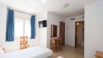 Un dormitorio con cama, escritorio, silla, espejo y televisor.