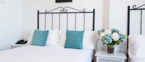 A neatly arranged hotel room with a bed, a bedside table with a phone, and a nightstand with a vase of flowers.