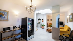 A modern hotel lobby with a microwave, coffee machine, and a beverage vending machine. There is a yellow sofa and black chairs in the seating area. - Hotel Mediterraneo by Croma (Estepona)