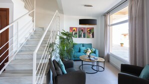 A modern living room with a staircase, a sofa, a coffee table, and a large window with curtains. - Hotel Mediterraneo by Croma (Estepona)