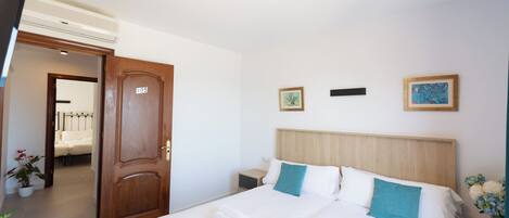 A hotel room with a double bed, two bedside tables, a wooden door, and a wall-mounted air conditioner.