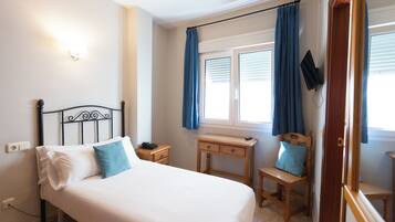 A bedroom with a bed, a desk, a chair, and a TV mounted on the wall.