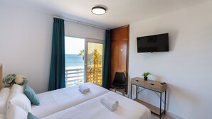 A hotel room with two beds, a TV, a desk, and a view of the sea. - Hotel Mediterraneo by Croma (Estepona)