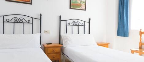 Una habitación con dos camas individuales, una mesita de noche con lámpara y dos cuadros en la pared.
