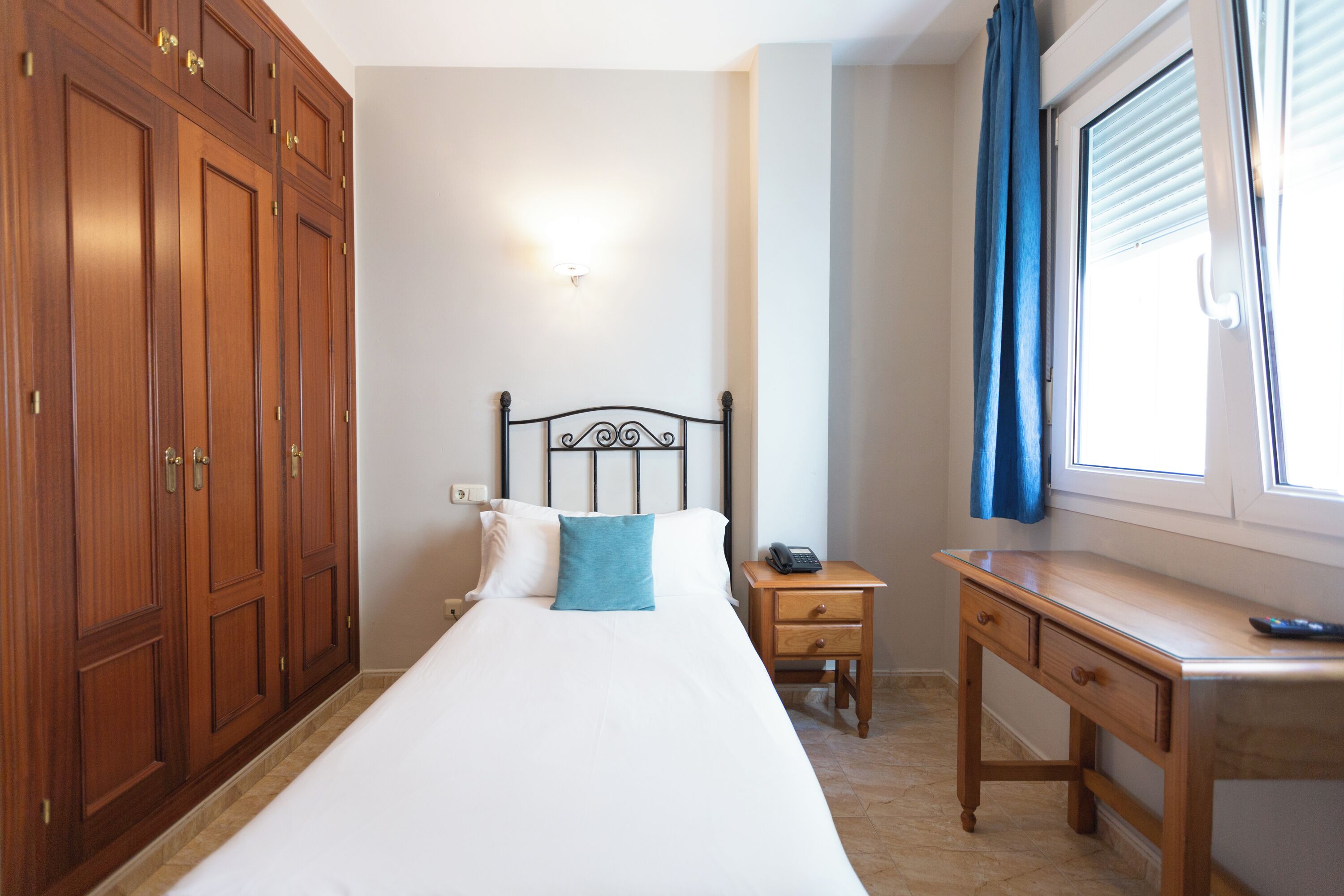 Ein Schlafzimmer mit Bett, Holzschrank, Nachttisch und Schreibtisch.