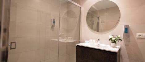 A modern bathroom with a glass-enclosed shower, a dark-toned vanity, and a round mirror.