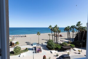 A beach view with palm trees, a parking area, and a building with a sign. - Hotel Mediterraneo by Croma (Estepona)