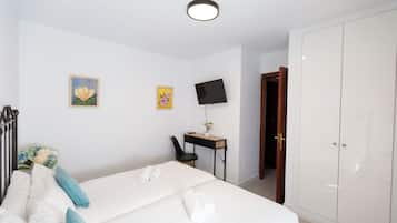 A hotel room with a bed, a desk with a computer, a TV, and a wardrobe.