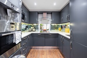 A modern kitchen with stainless steel appliances, dark cabinetry, and a wooden floor.