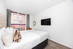 Habitación de hotel con cama, televisión, escritorio y ventana con cortinas.