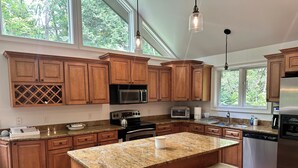 Eine geräumige Küche mit Holzschränken, Granit Arbeitsplatten, einem Edelstahlkühlschrank und einer großen Kochinsel mit Barhocker.