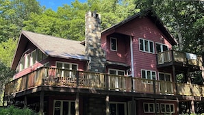 Eine zweistöckige Holzhütte mit einem Steinofen, einer Holzterrasse und zahlreichen Fenstern.