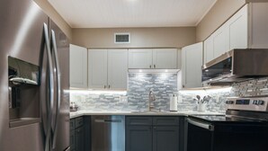 A modern kitchen with stainless steel appliances, white cabinets, and a tiled backsplash. - Salty Shores Secluded Oasis (Englewood)