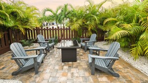 A patio with four Adirondack chairs and a square table, surrounded by palm trees and a wooden fence. - Salty Shores Secluded Oasis (Englewood)