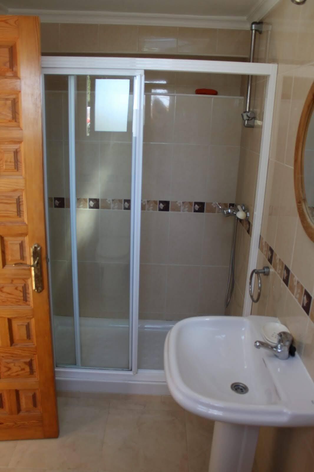 A bathroom with a glass shower door, a sink, and a wooden door.