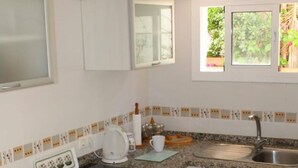 A kitchen with white cabinets, a granite countertop, a black stove, and a window with a view of greenery. - Apartamento Paco Romo (Nerja)