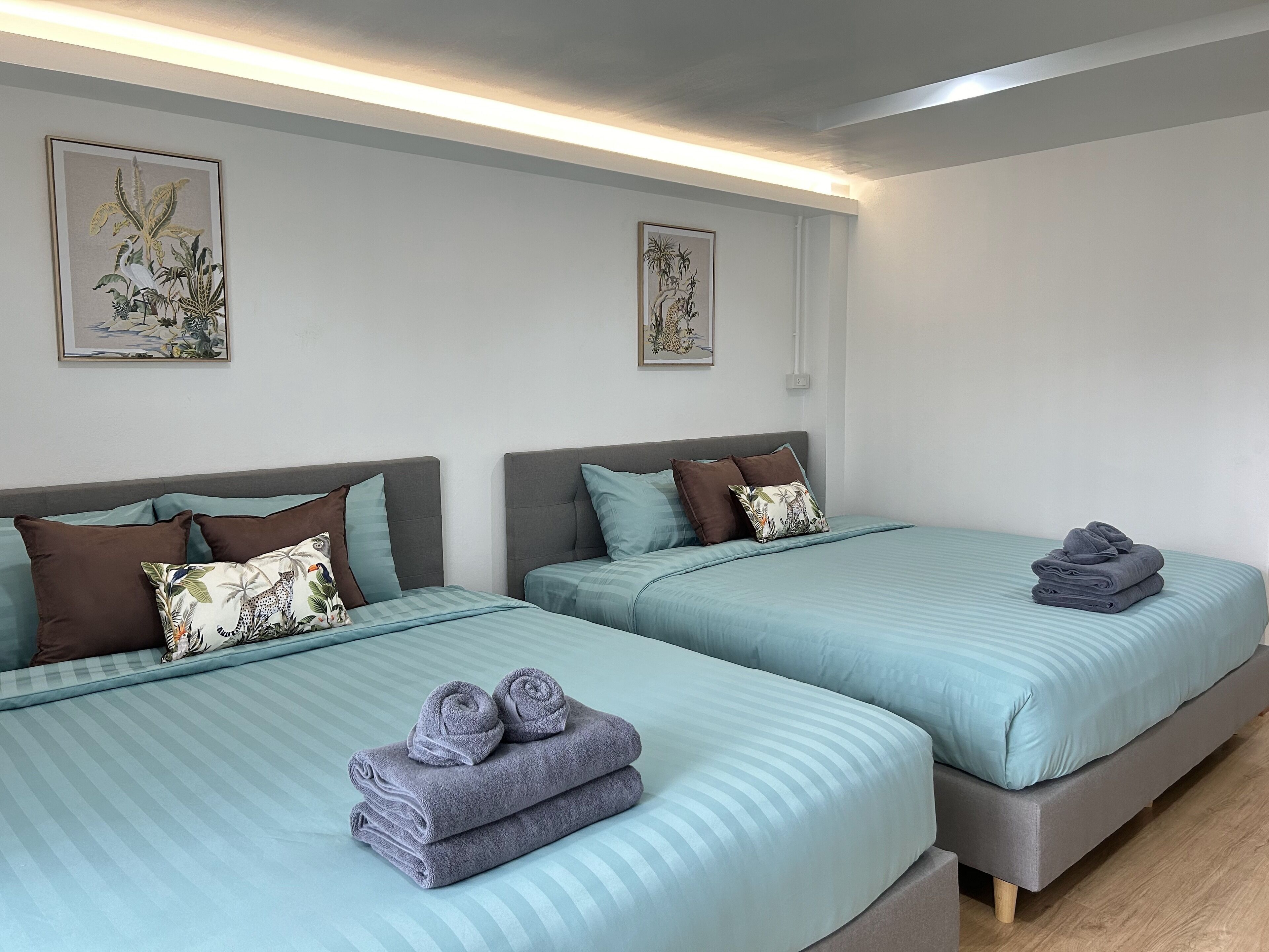 Camera d'albergo con due letti, ciascuno con una testiera grigia, biancheria azzurra e cuscini decorativi. Alle pareti, stampe botaniche incorniciate.