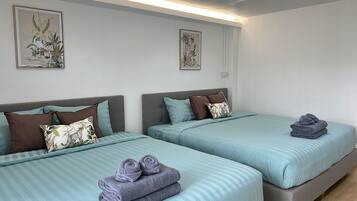 Camera d'albergo con due letti, ciascuno con una testiera grigia, biancheria azzurra e cuscini decorativi. Alle pareti, stampe botaniche incorniciate.