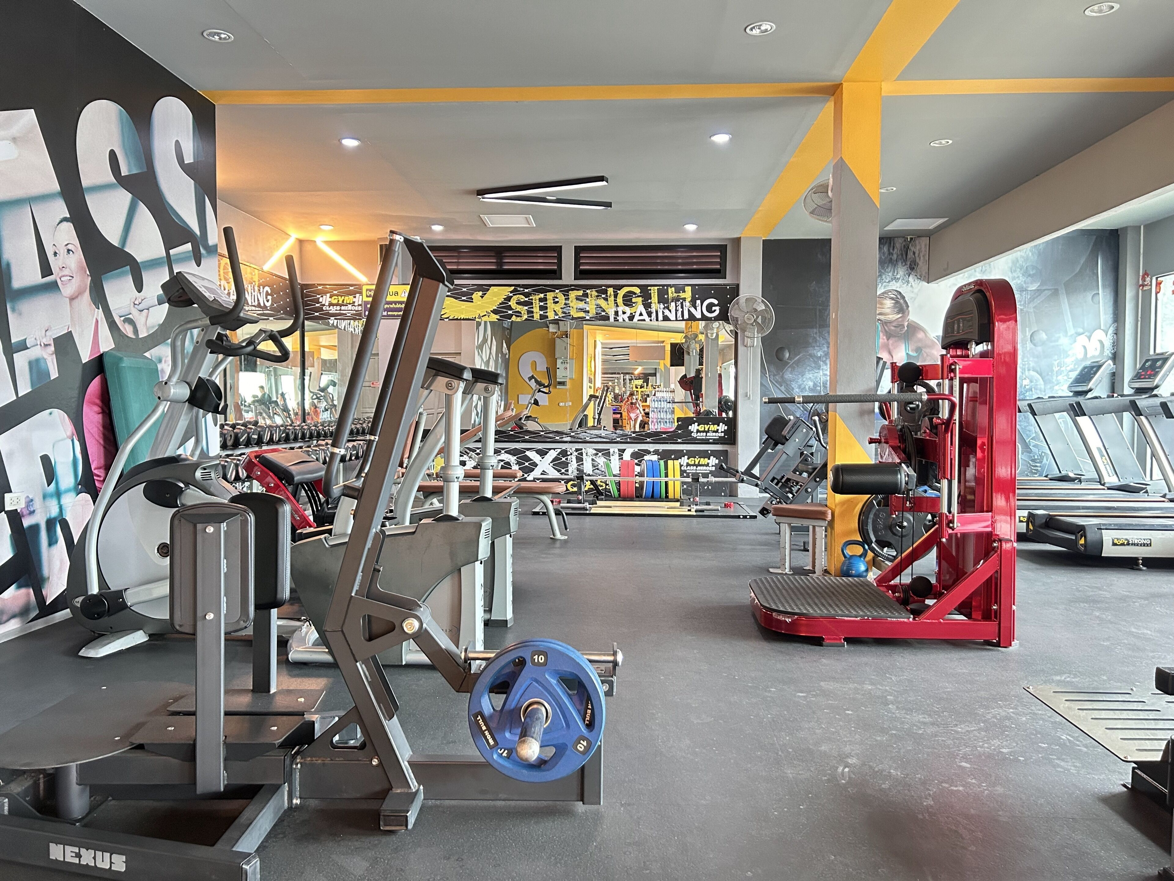 Ein Fitnessstudio mit Krafttrainingsgeräten, Laufbändern und einer Spiegelwand.
