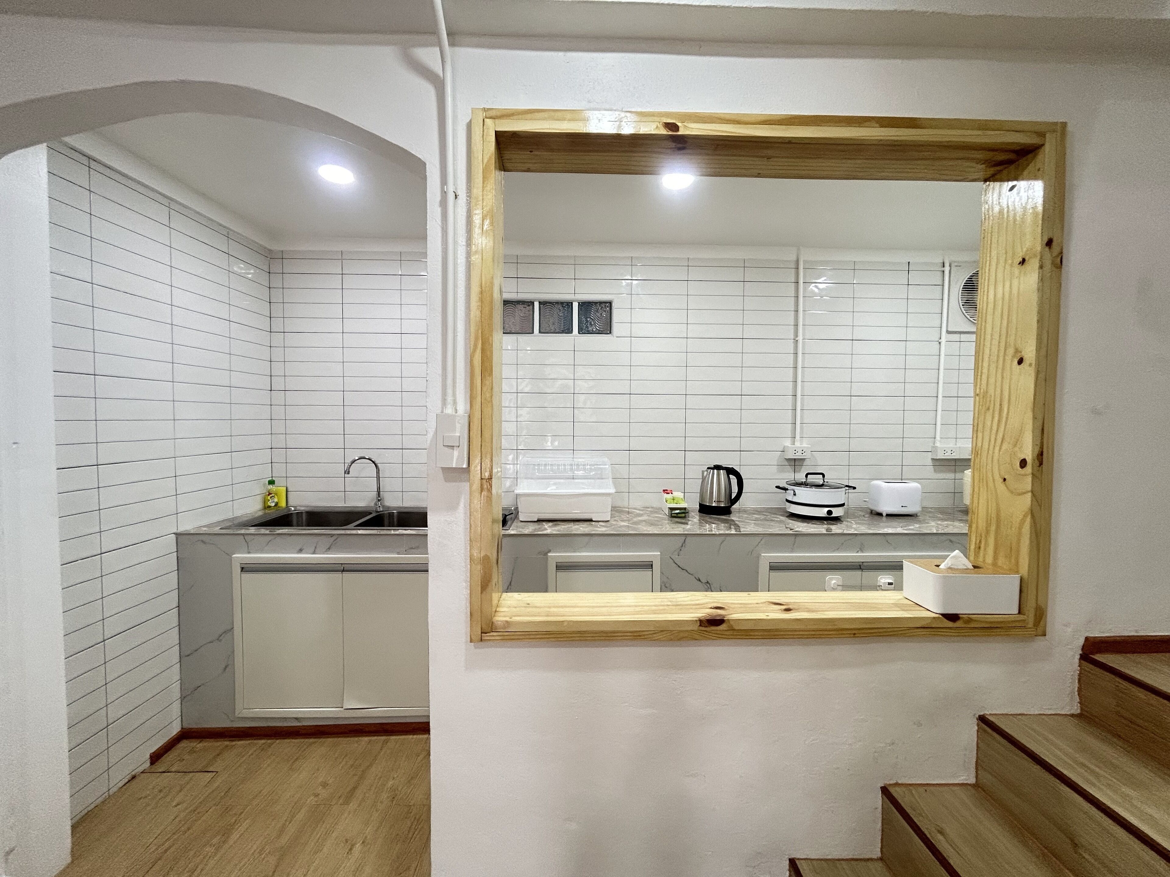 A compact kitchen with white tiled walls, a wooden-framed mirror, a sink, a stove, and a countertop with various appliances.