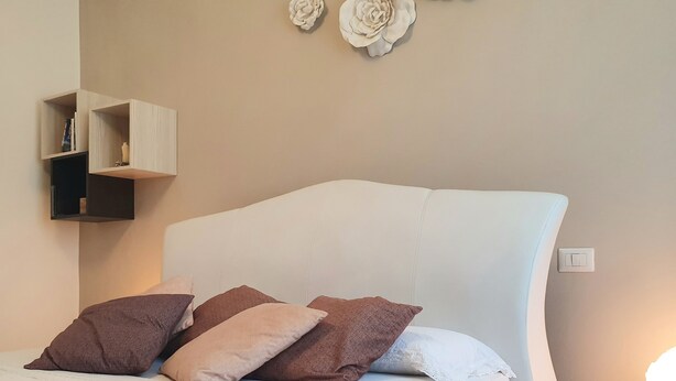 A neatly made bed with pillows, a bedside table with a lamp, and wall-mounted shelves. - Lemon Sunshine Ciampino (Ciampino)