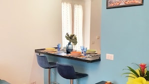 Een moderne keuken met een bar, twee barkrukken, een eettafel en een decoratieve plant.