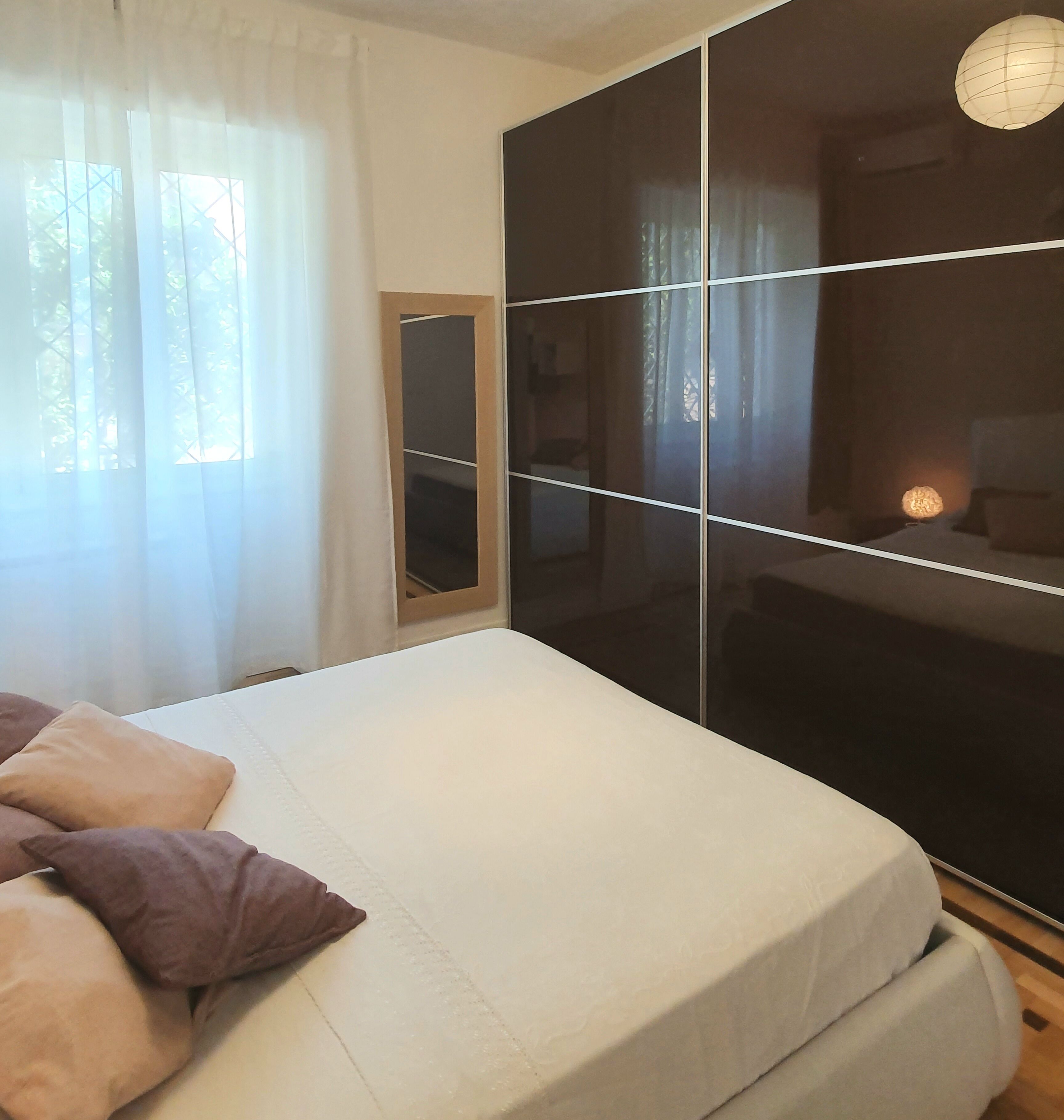A bedroom with a bed, a wardrobe, and a window with curtains.